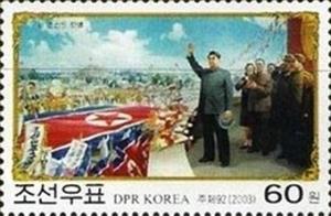 Colnect-2415-355-Kim-saluting-marchers-carrying-DPRK-flag.jpg